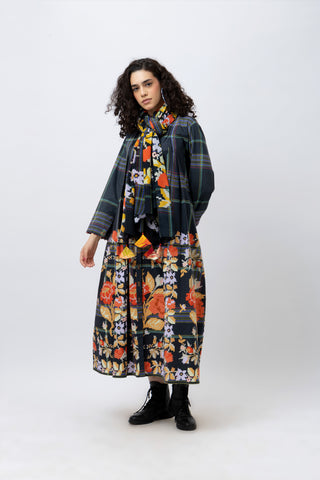 Woman wearing a long floral dress with a plaid coat and colorful scarf on a white background